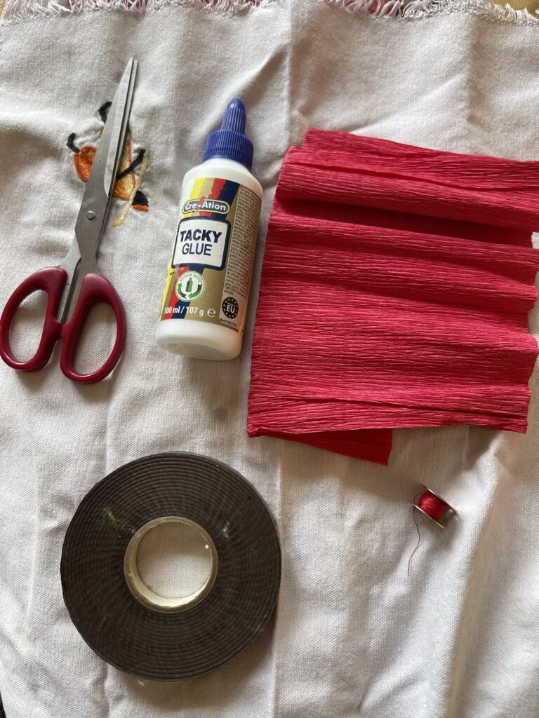 Materiales necesarios para hacer una rosa de papel crepé: papel crepé rojo y verde, tijeras, pegamento, hilo, cinta floral y una rama