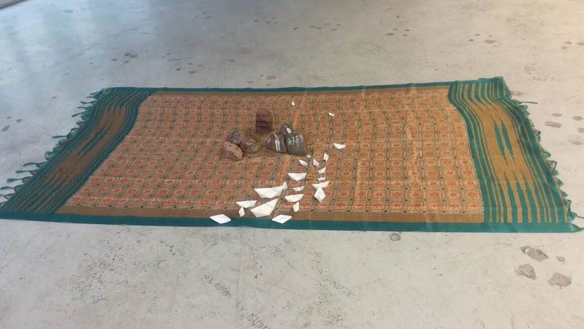 Piedras falsas de papel maché con rostros de prisioneros dibujados junto a una pequeña instalación de alfombra de oración