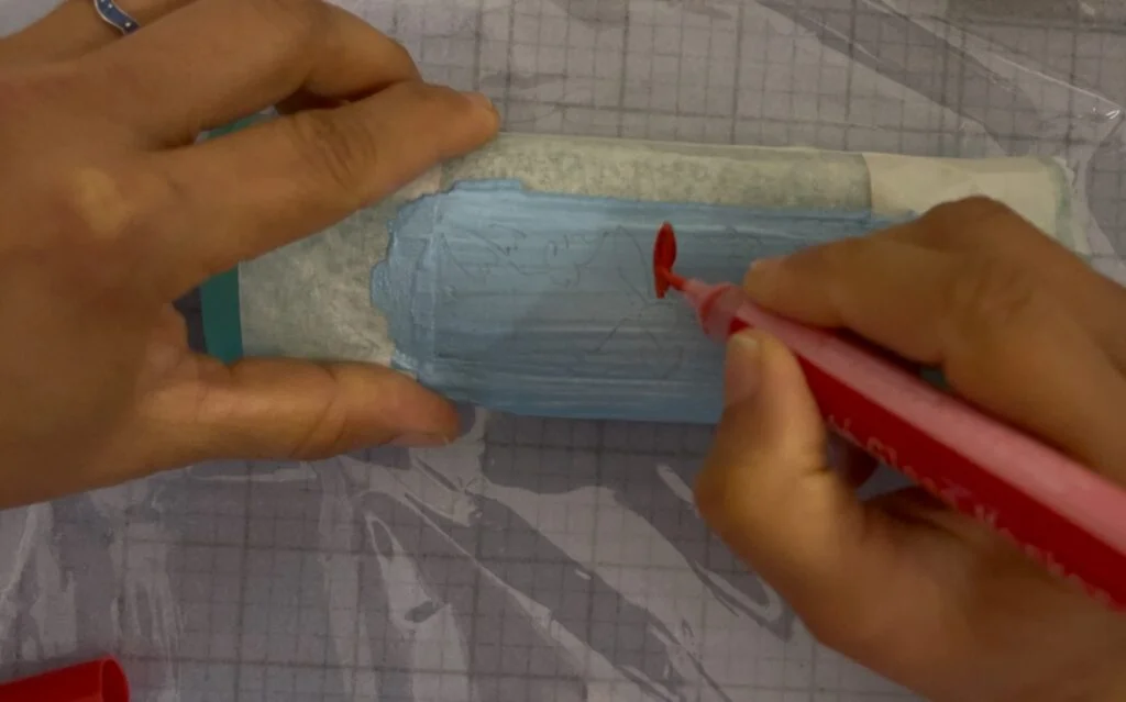 Peinture des premières zones de couleur du motif sur la boîte à lunettes optiques avec un petit pinceau