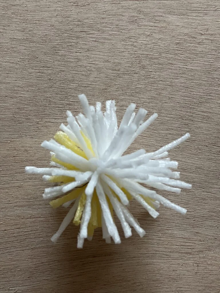 Application de colle à la base du pompon de Kadam avant de le fixer sur une branche naturelle