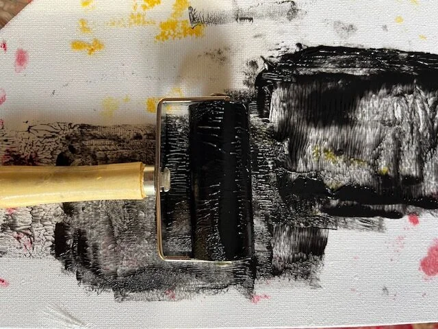 Brayer rolling a thin even layer of black ink over the raised surface of a carved linoleum block
